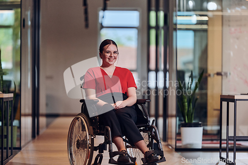 Image of A modern young businesswoman in a wheelchair is surrounded by an inclusive workspace with glass-walled offices, embodying determination and innovation in the business world