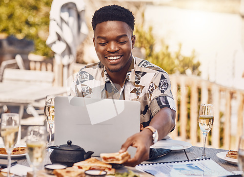 Image of Man working on a laptop while eating lunch at an outdoor restaurant with 5g service in the city. Casual employee doing research on internet with a computer while having sandwich and champagne at cafe