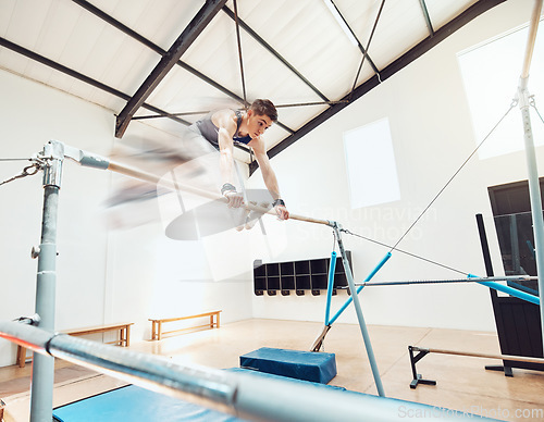 Image of Gymnastics, man and sports with a gymnast swinging on a horizontal bar inside of a gym for fitness, training and workout. Sport, exercise and practice with an athlete holding onto parallel bars