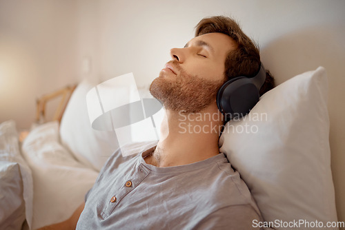 Image of Relax, meditation and resting man listening to music on his wireless headphones while relaxing on his bed at home. Relaxed and calm male dreaming sleeping due to audiobook or podcast in his bedroom