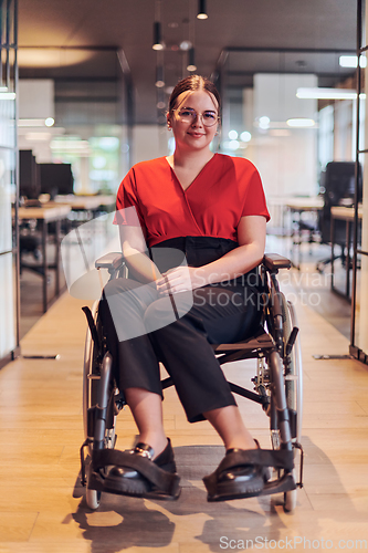 Image of A modern young businesswoman in a wheelchair is surrounded by an inclusive workspace with glass-walled offices, embodying determination and innovation in the business world