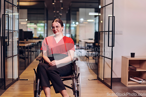 Image of A modern young businesswoman in a wheelchair is surrounded by an inclusive workspace with glass-walled offices, embodying determination and innovation in the business world