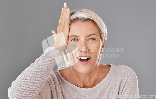 Image of Thinking, idea or memory with a senior woman knocking her head with her hand to remember or forget in studio on a grey background. Face portrait of a model with grey hair having a light bulb moment