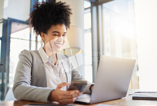 Image of Happy corporate employee texting on a phone while working on a laptop in an office, reading email. Young professional assistant multitasking to complete an online task, efficient time management