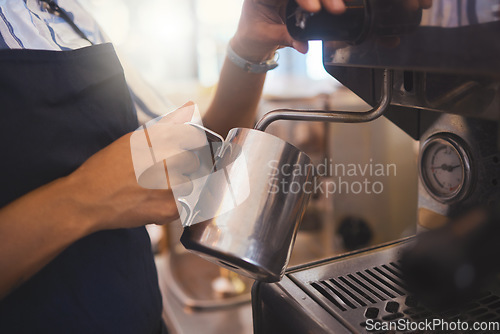 Image of Coffee shop, barista and waitress working in a cafe and pouring a fresh drink in a restaurant while in an apron. Closeup of a hand foaming or steaming milk in the service and hospitality industry.