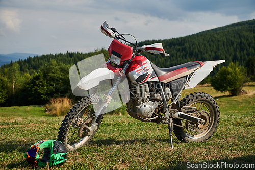 Image of A professional motocross standing poised in a meadow, fully geared up and ready for a competitive race, with the anticipation of adrenaline-fueled excitement in the air.