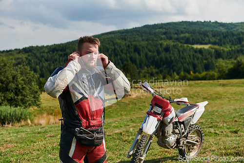 Image of A professional motocross rider, clad in a full suit, gloves, and backpack, prepares for a daring adventure through the forest, geared up for an adrenaline-pumping off-road journey