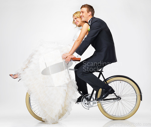 Image of Happy, wedding and couple on a bicycle against a white background, after getting married together. Love, young bride and groom in dress and suit, cycling on a bike in marriage happiness or bliss