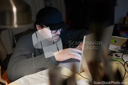 Image of A close-up shot of a man using a laptop in a dimly lit room, engrossed in his digital work during the late hours of the night