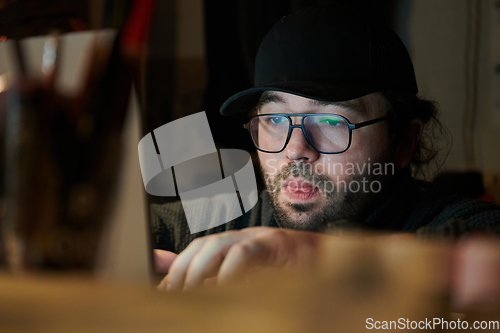 Image of A close-up shot of a man using a laptop in a dimly lit room, engrossed in his digital work during the late hours of the night