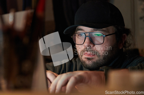 Image of A close-up shot of a man using a laptop in a dimly lit room, engrossed in his digital work during the late hours of the night