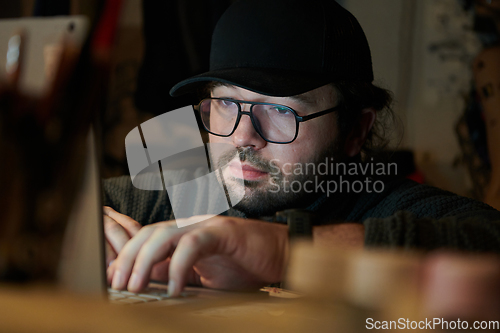 Image of A close-up shot of a man using a laptop in a dimly lit room, engrossed in his digital work during the late hours of the night