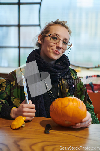 Image of A modern blonde woman in military uniform is carving spooky pumpkins with a knife for Halloween night