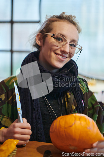 Image of A modern blonde woman in military uniform is carving spooky pumpkins with a knife for Halloween night