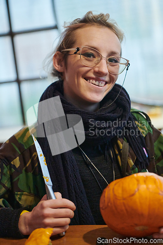 Image of A modern blonde woman in military uniform is carving spooky pumpkins with a knife for Halloween night