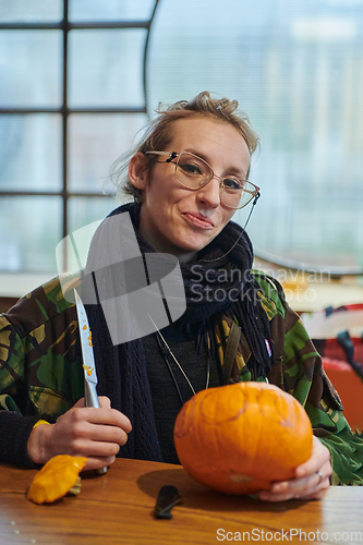 Image of A modern blonde woman in military uniform is carving spooky pumpkins with a knife for Halloween night