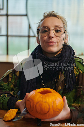 Image of A modern blonde woman in military uniform is carving spooky pumpkins with a knife for Halloween night