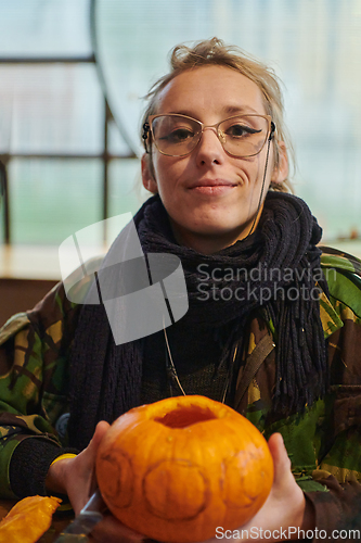 Image of A modern blonde woman in military uniform is carving spooky pumpkins with a knife for Halloween night