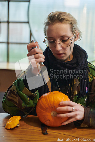 Image of A modern blonde woman in military uniform is carving spooky pumpkins with a knife for Halloween night