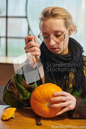 Image of A modern blonde woman in military uniform is carving spooky pumpkins with a knife for Halloween night