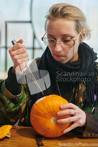 Image of A modern blonde woman in military uniform is carving spooky pumpkins with a knife for Halloween night