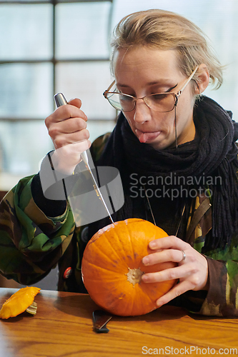 Image of A modern blonde woman in military uniform is carving spooky pumpkins with a knife for Halloween night