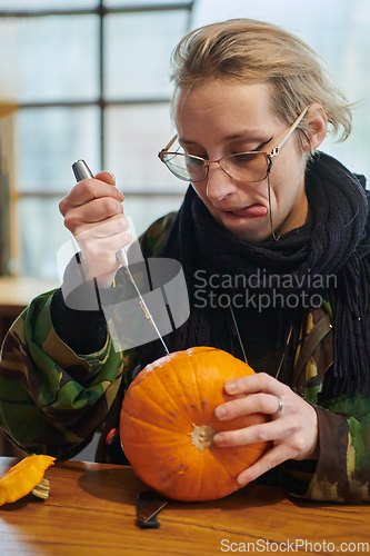 Image of A modern blonde woman in military uniform is carving spooky pumpkins with a knife for Halloween night