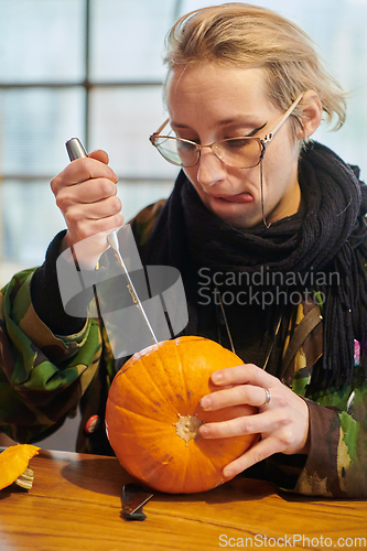 Image of A modern blonde woman in military uniform is carving spooky pumpkins with a knife for Halloween night