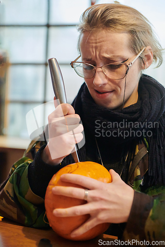 Image of A modern blonde woman in military uniform is carving spooky pumpkins with a knife for Halloween night