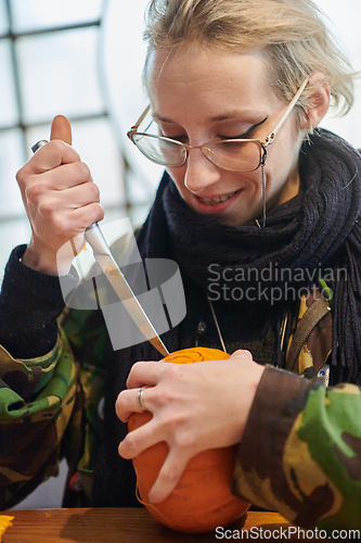 Image of A modern blonde woman in military uniform is carving spooky pumpkins with a knife for Halloween night