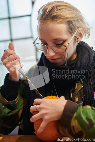 Image of A modern blonde woman in military uniform is carving spooky pumpkins with a knife for Halloween night