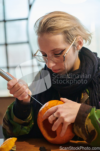 Image of A modern blonde woman in military uniform is carving spooky pumpkins with a knife for Halloween night