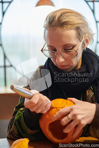 Image of A modern blonde woman in military uniform is carving spooky pumpkins with a knife for Halloween night