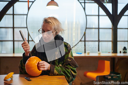 Image of A modern blonde woman in military uniform is carving spooky pumpkins with a knife for Halloween night