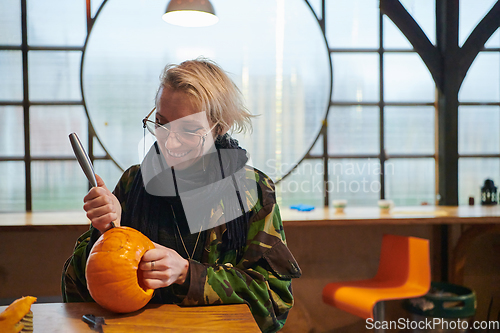 Image of A modern blonde woman in military uniform is carving spooky pumpkins with a knife for Halloween night