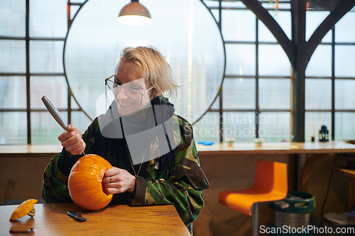 Image of A modern blonde woman in military uniform is carving spooky pumpkins with a knife for Halloween night