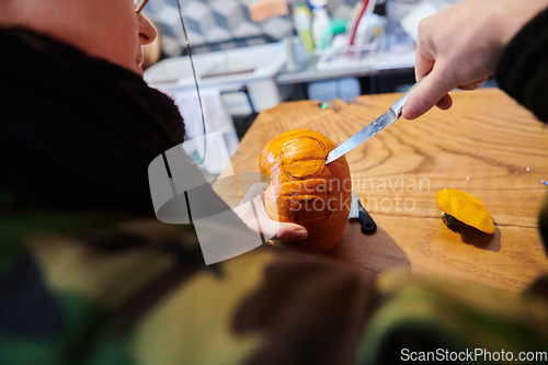 Image of A modern blonde woman in military uniform is carving spooky pumpkins with a knife for Halloween night