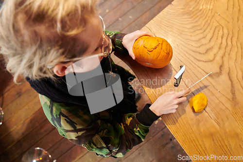 Image of A modern blonde woman in military uniform is carving spooky pumpkins with a knife for Halloween night