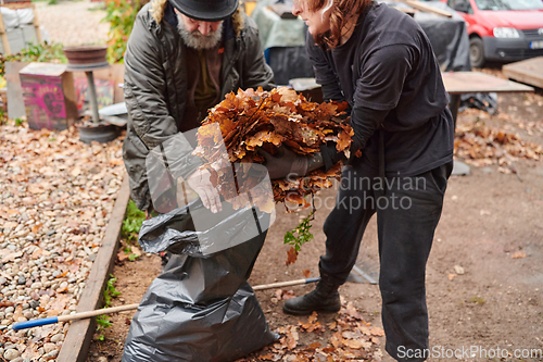 Image of Father-daughter duo bonding in the garden as they work together to collect fallen leaves and fill up a bag on a crisp autumn day.