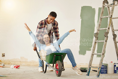 Image of DIY, painting and happy couple smile while moving into new home, real estate property house or building. Love, creative man and woman on wheelbarrow interior design and renovation work on room wall