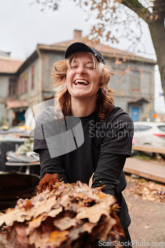 Image of A stylish, modern young woman takes on the role of a garden caretaker, diligently collecting old, dry leaves and cleaning up the yard in an eco-conscious manner