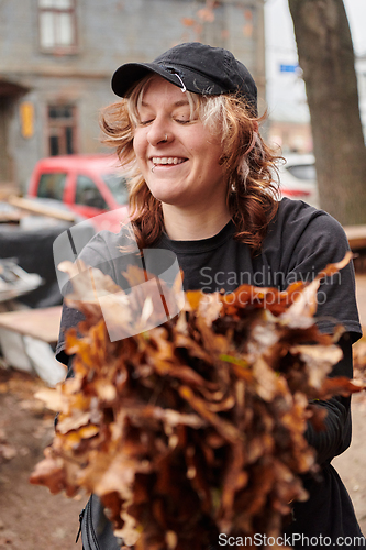 Image of A stylish, modern young woman takes on the role of a garden caretaker, diligently collecting old, dry leaves and cleaning up the yard in an eco-conscious manner