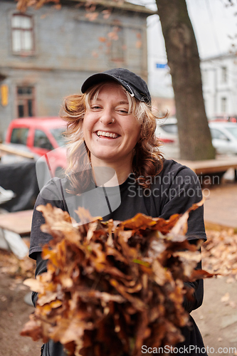 Image of A stylish, modern young woman takes on the role of a garden caretaker, diligently collecting old, dry leaves and cleaning up the yard in an eco-conscious manner