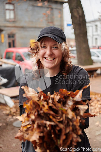 Image of A stylish, modern young woman takes on the role of a garden caretaker, diligently collecting old, dry leaves and cleaning up the yard in an eco-conscious manner