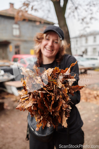 Image of A stylish, modern young woman takes on the role of a garden caretaker, diligently collecting old, dry leaves and cleaning up the yard in an eco-conscious manner