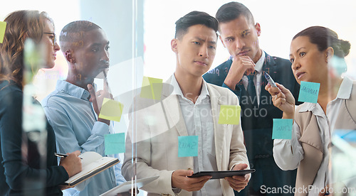 Image of Teamwork, strategy and collaboration with planning business people writing sticky notes on a board or window. Serious thinking and creative problem solving with diverse group on a innovation mission