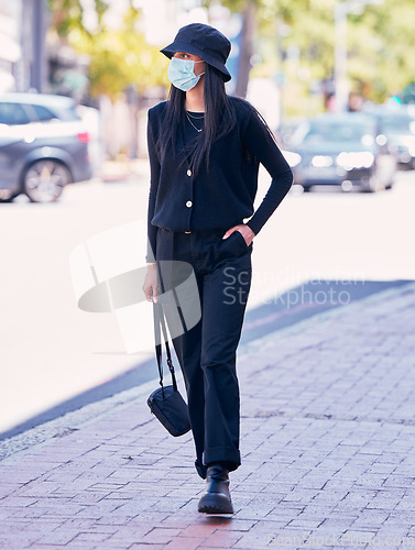 Image of City woman, on a sidewalk, with a mask on her face and walking down the road. Urban fashion, casual walk and covid protection, life in the new normal. Calm beauty, trendy girl walks on the pavement.