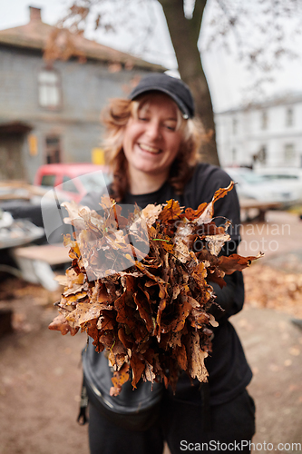 Image of A stylish, modern young woman takes on the role of a garden caretaker, diligently collecting old, dry leaves and cleaning up the yard in an eco-conscious manner