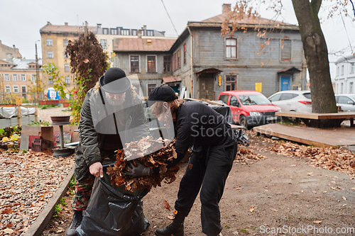 Image of Father-daughter duo bonding in the garden as they work together to collect fallen leaves and fill up a bag on a crisp autumn day.