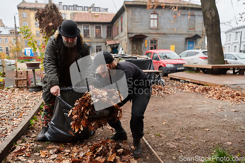 Image of Father-daughter duo bonding in the garden as they work together to collect fallen leaves and fill up a bag on a crisp autumn day.